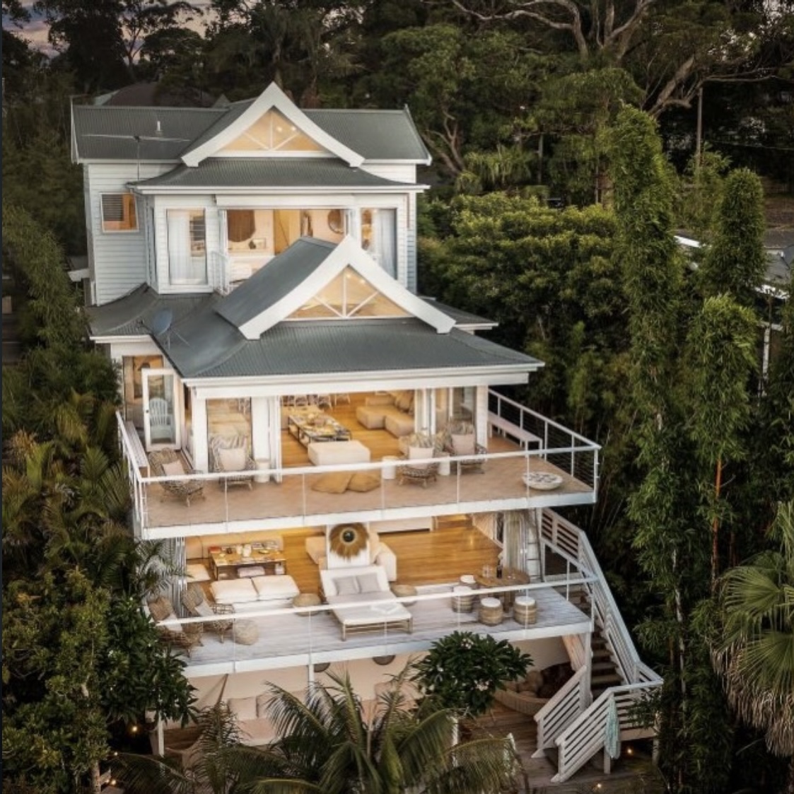 Dusk aerial view of all four levels of the property glowing with warm interiors and lush tree canopy