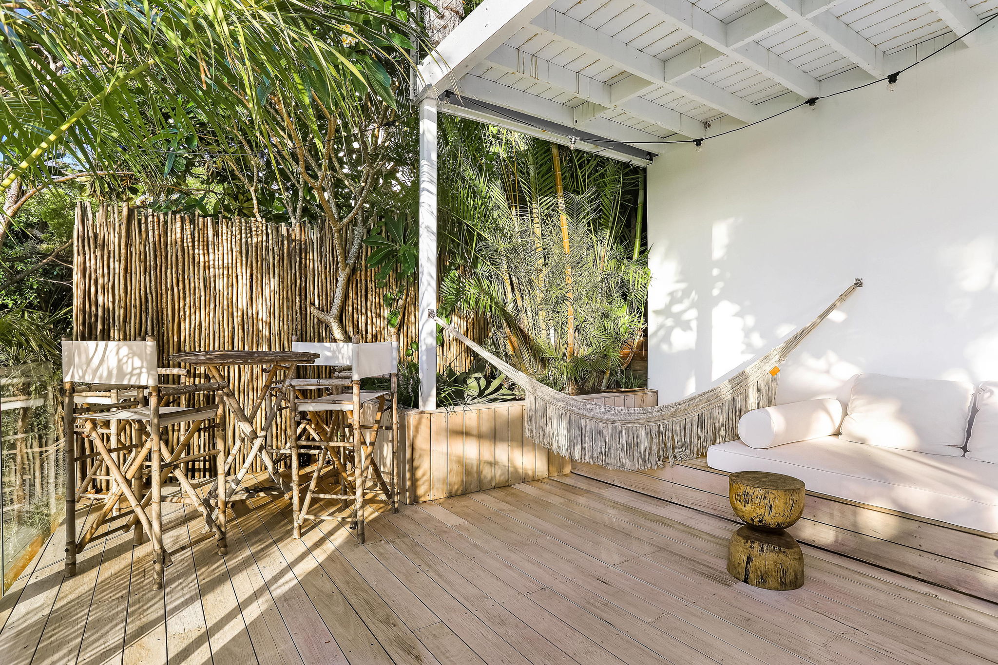 Timber deck with bamboo screen, rattan dining chairs and macrame hammock