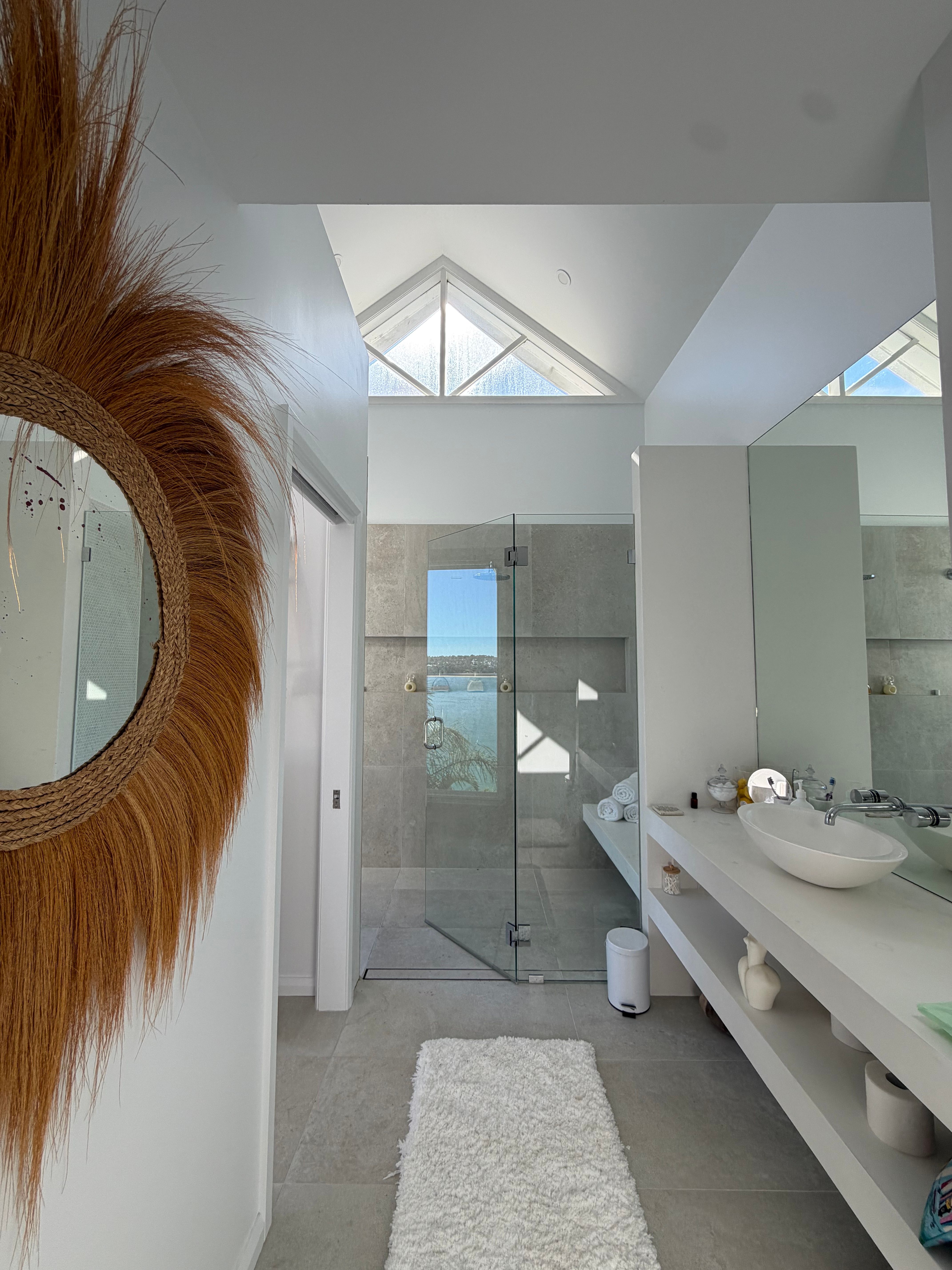 Bathroom with raffia sunburst mirror, glass shower with ocean view and triangular skylights