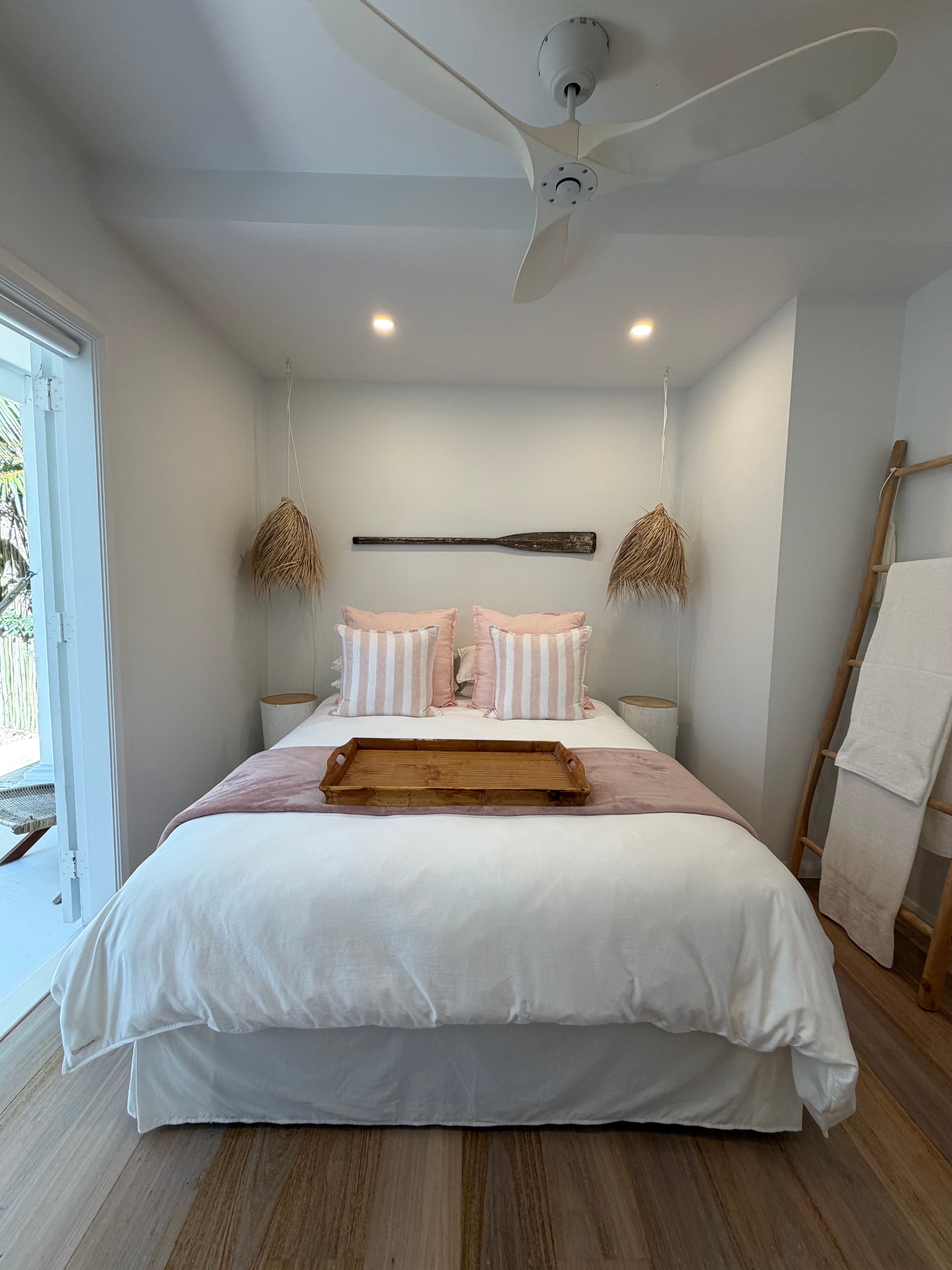 Pink bedroom wide shot with ceiling fan, towel ladder, rattan pendants and oar wall art