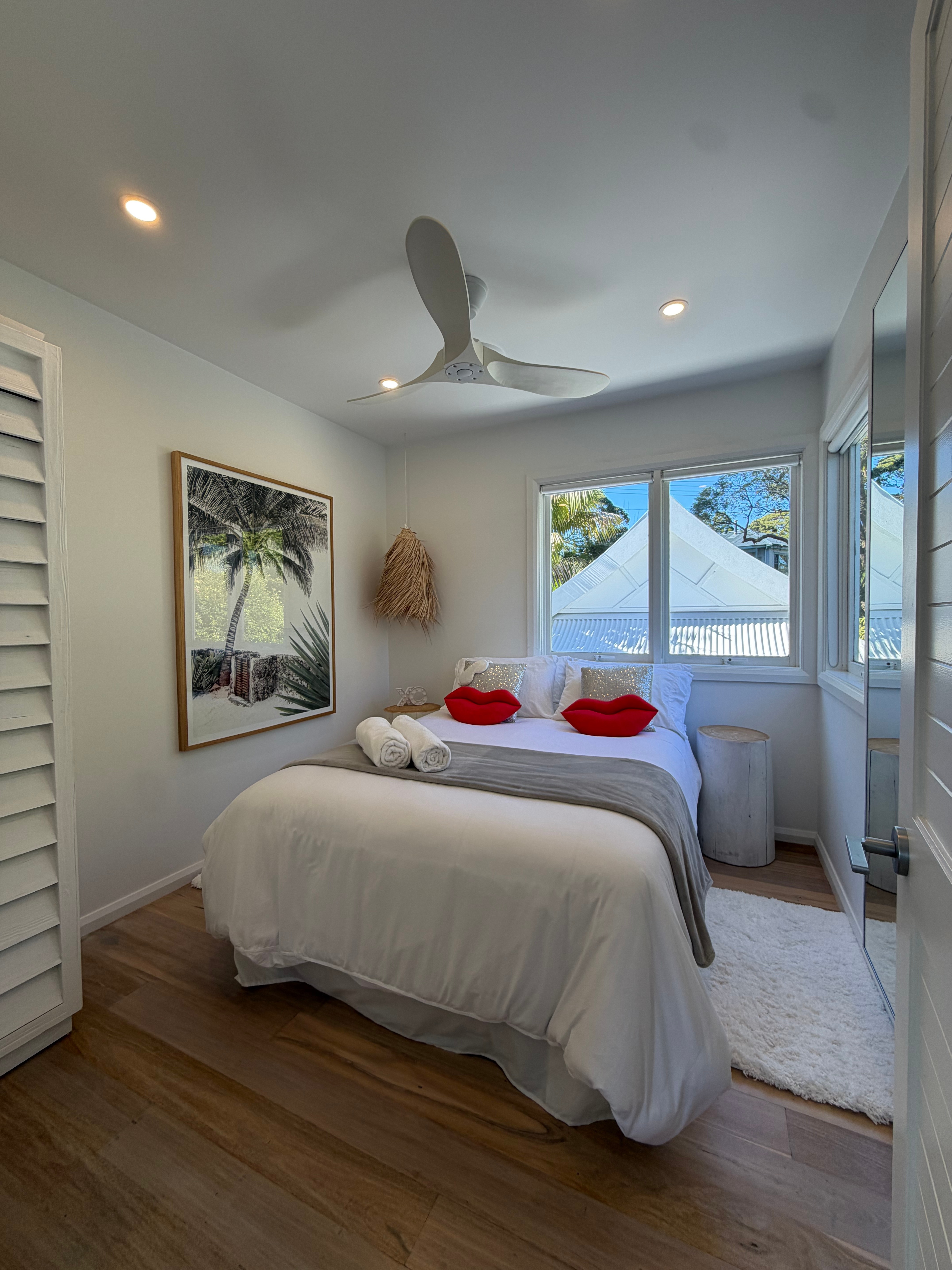 Bright bedroom with white bed, red lip pillows and palm tree artwork