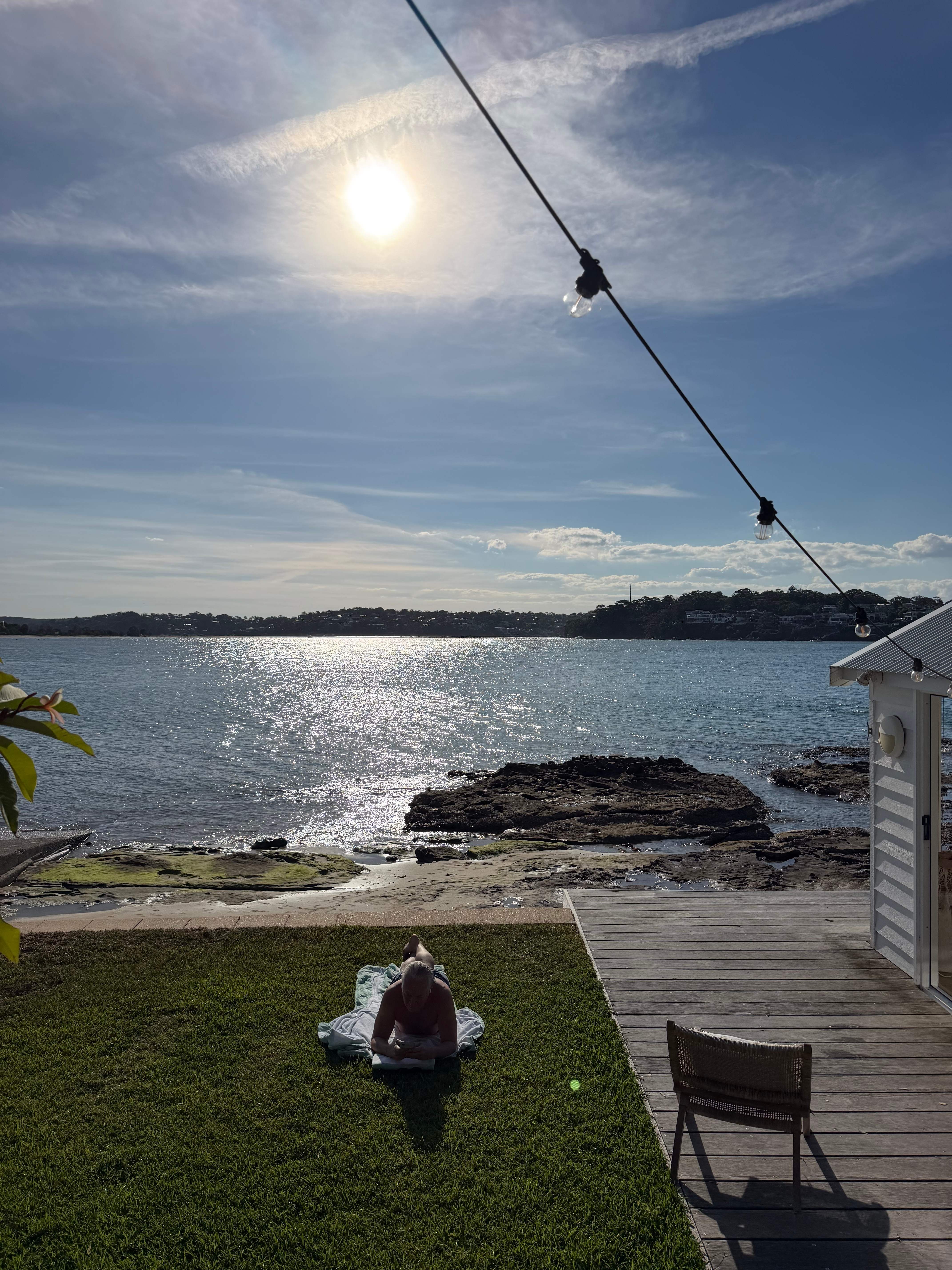 Person relaxing on waterfront lawn with festoon lights and beach cabin