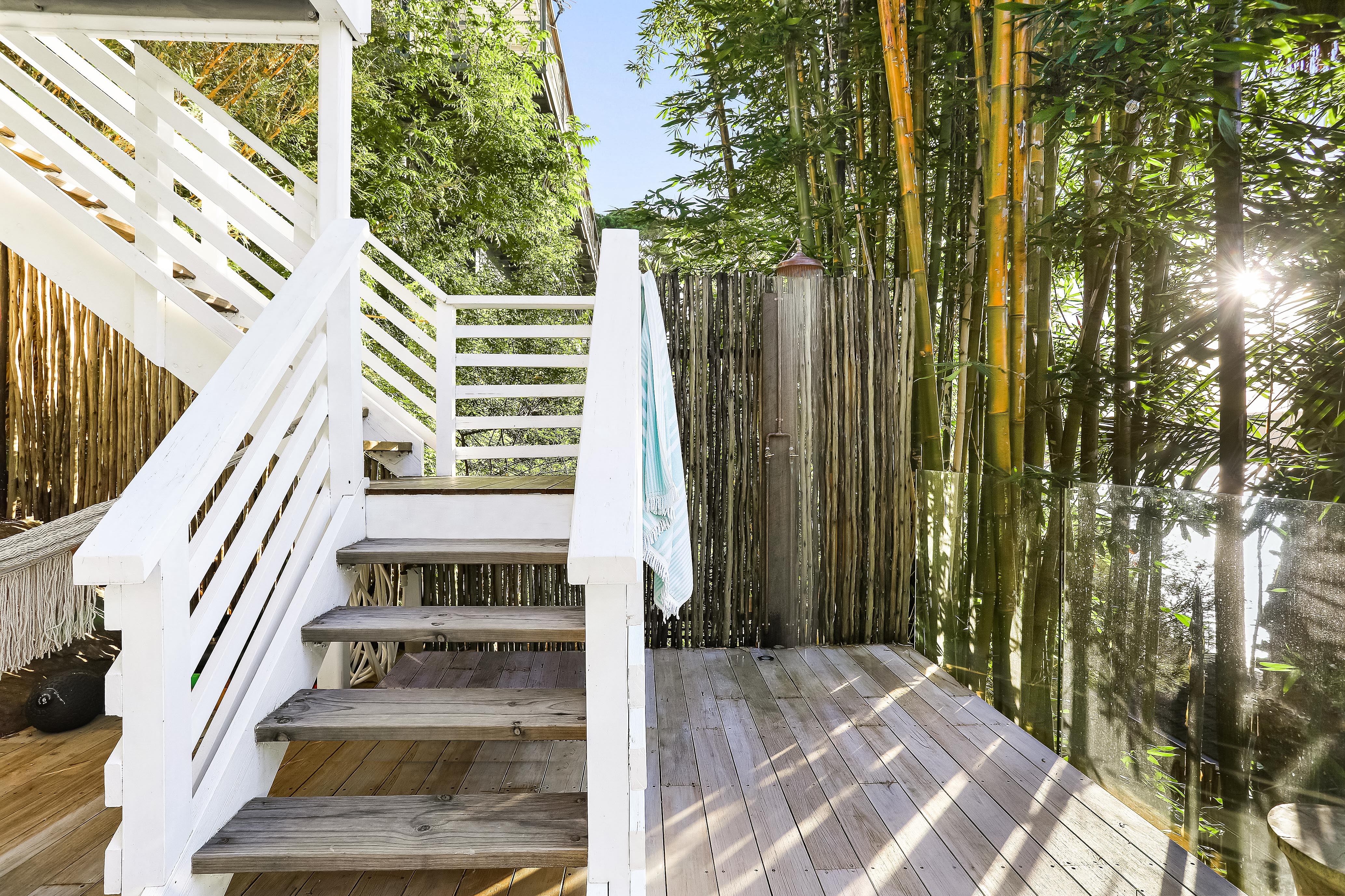 Outdoor shower enclosed by bamboo screen with festoon lights and deck stairs
